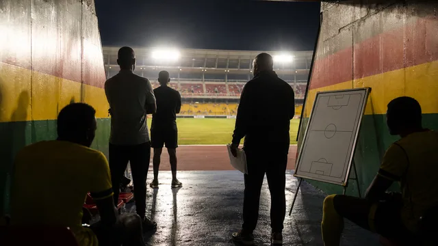 Generic Ghana football staff and players waiting in a stadium tunnel beside a blank tactical board